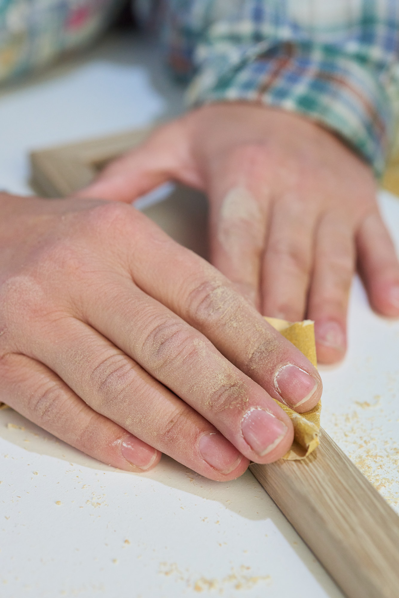 close-up image of dusty hands sanding an oak picture frame